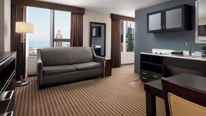 Een hotelkamer met een bank, een bureau, een flatscreen televisie, een lamp en uitzicht op de stad.