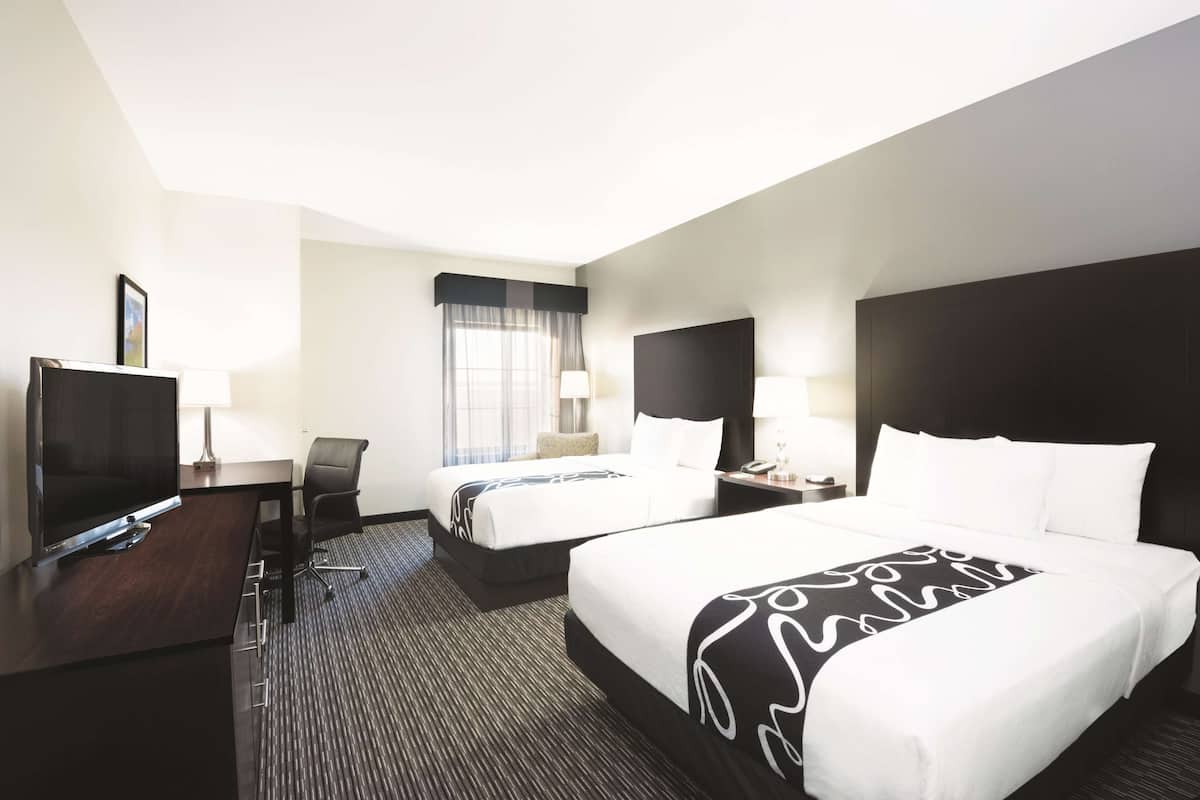 A hotel room with two beds, a desk with a TV, and a window with curtains.