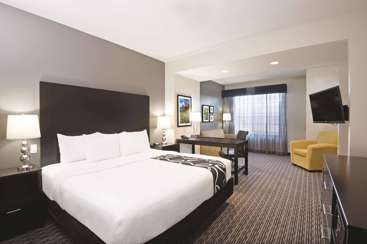 A hotel room with a large bed, a desk, a chair, a TV, and a window with curtains.