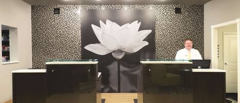 Un mostrador de recepción con un gran mural de flor de loto, dos mostradores con frentes de vidrio y una persona detrás del mostrador.
