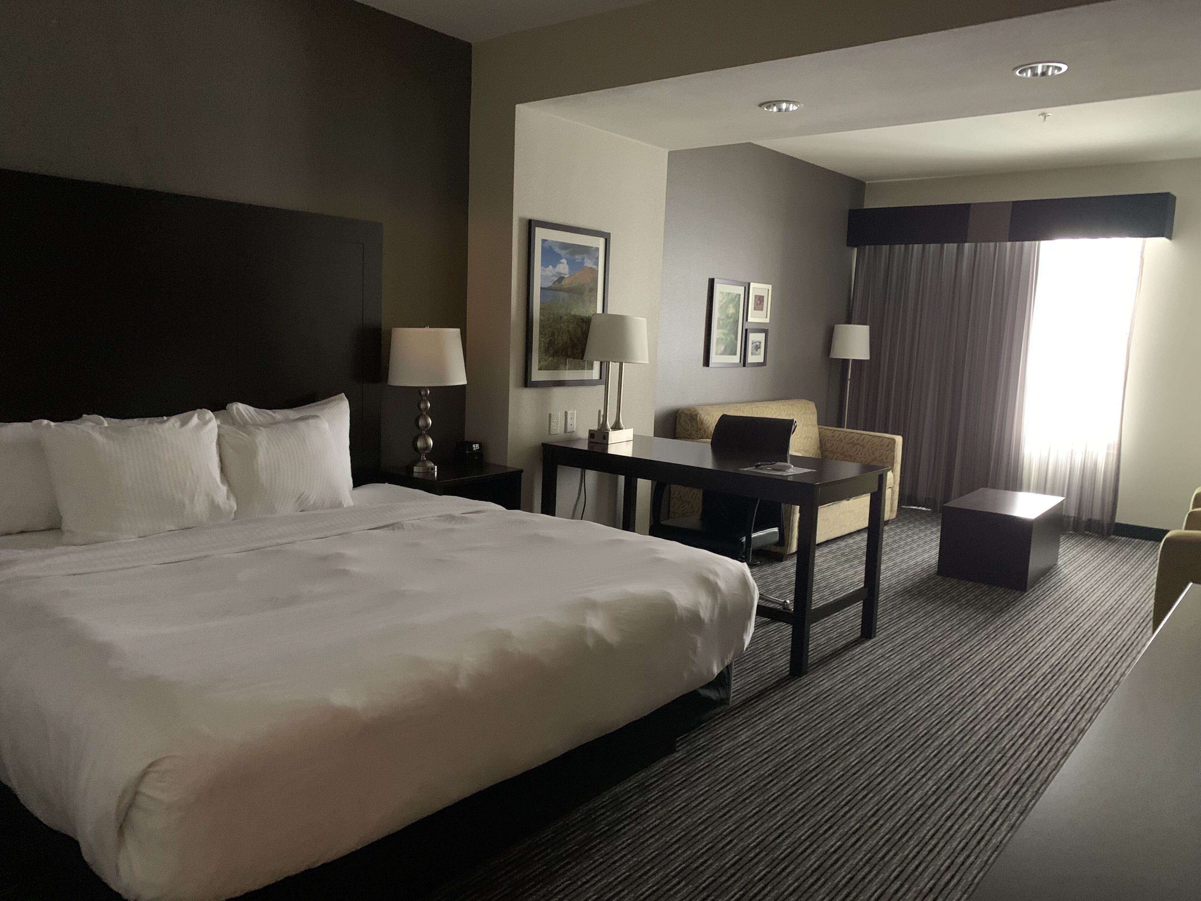 A hotel room with a large bed, a desk, a chair, and a small table.