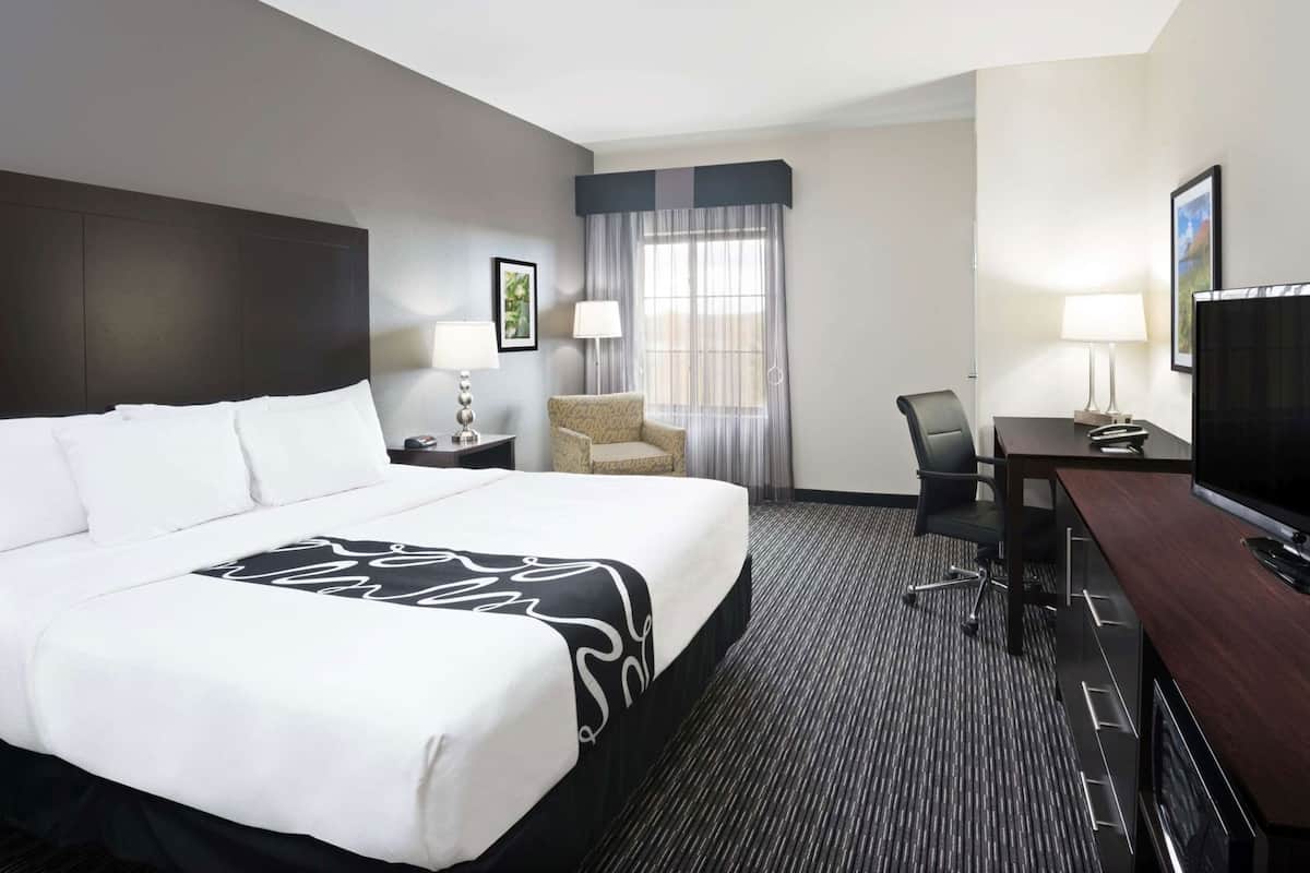 A hotel room with a large bed, a desk with a TV, a chair, a lamp, and a window with curtains.