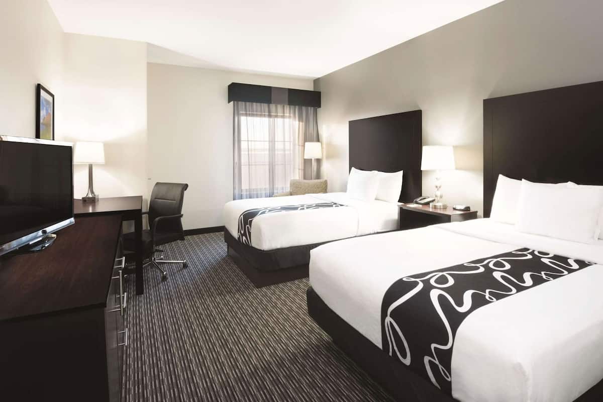 A hotel room with two beds, a desk with a TV, a chair, and a window with curtains.