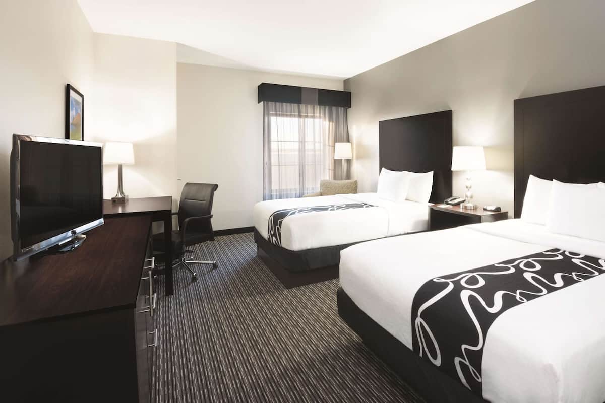 A hotel room with two beds, a desk with a TV, a chair, and a window with curtains.
