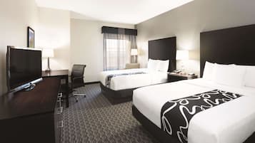 A hotel room with two beds, a desk with a TV, a chair, and a window with curtains.