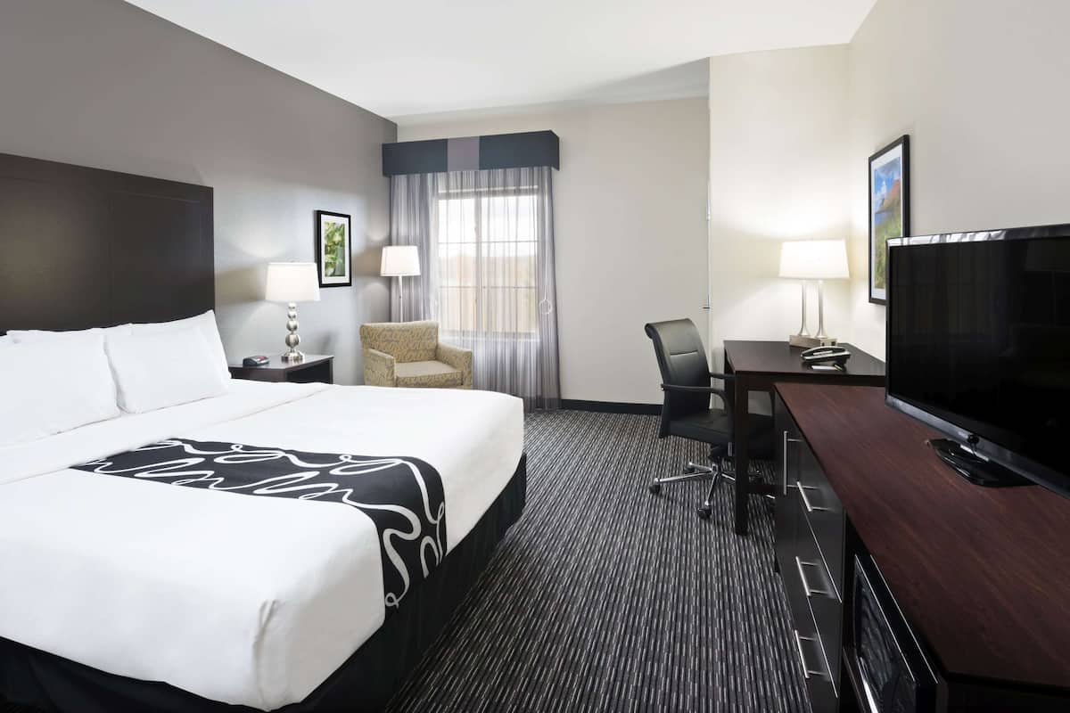A hotel room with a large bed, a desk with a TV, a chair, a lamp, and a window with curtains.