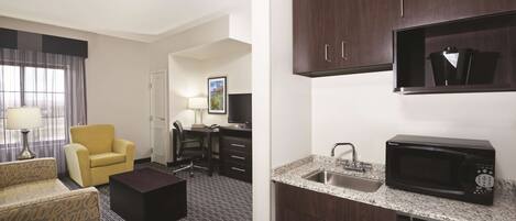A hotel room with a living area, a kitchenette, and a separate office space.