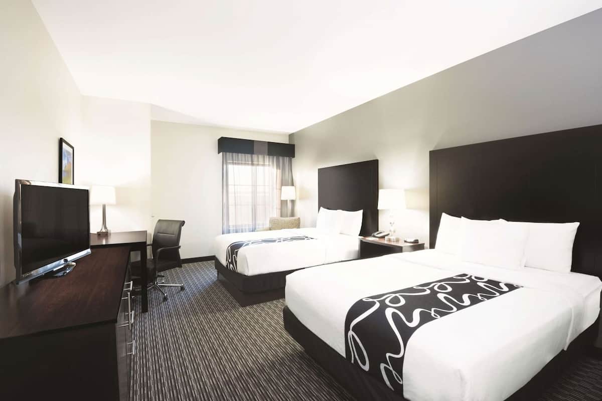 A hotel room with two beds, a desk with a TV, a chair, a window with curtains, and a nightstand with a lamp.