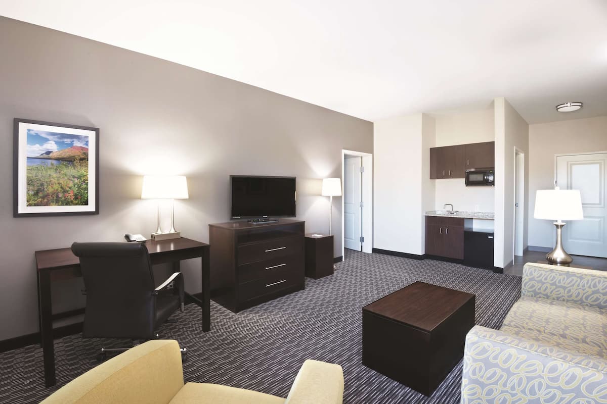 A hotel room with a desk, TV, sofa, and kitchenette.