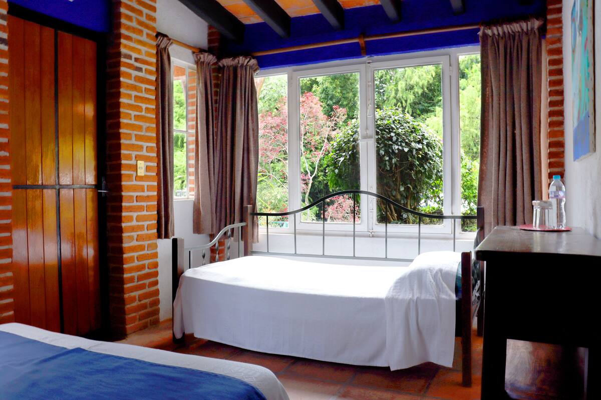 A bedroom with a large window, a bed, a table, and a chair.