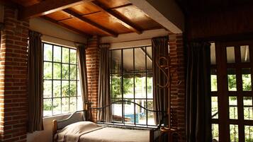 A room with a bed, a window with curtains, and a view of greenery outside.