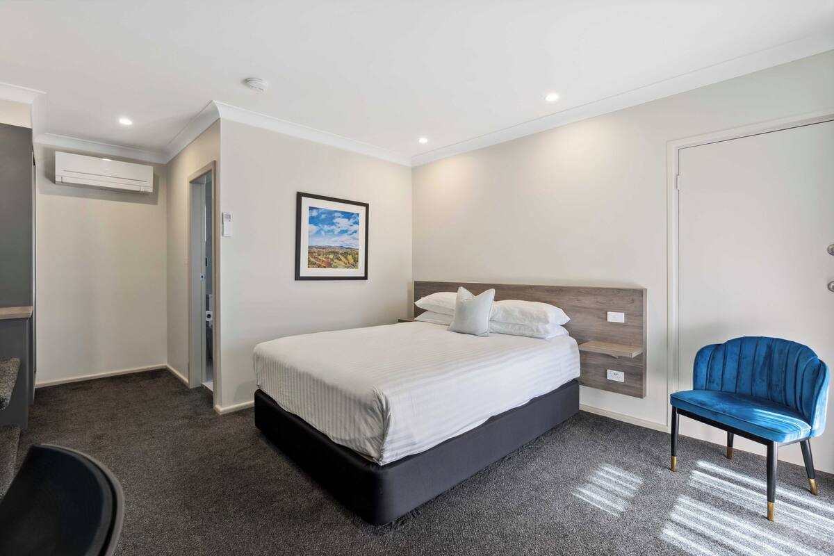 A modern bedroom with a large bed, a blue chair, and a picture on the wall.