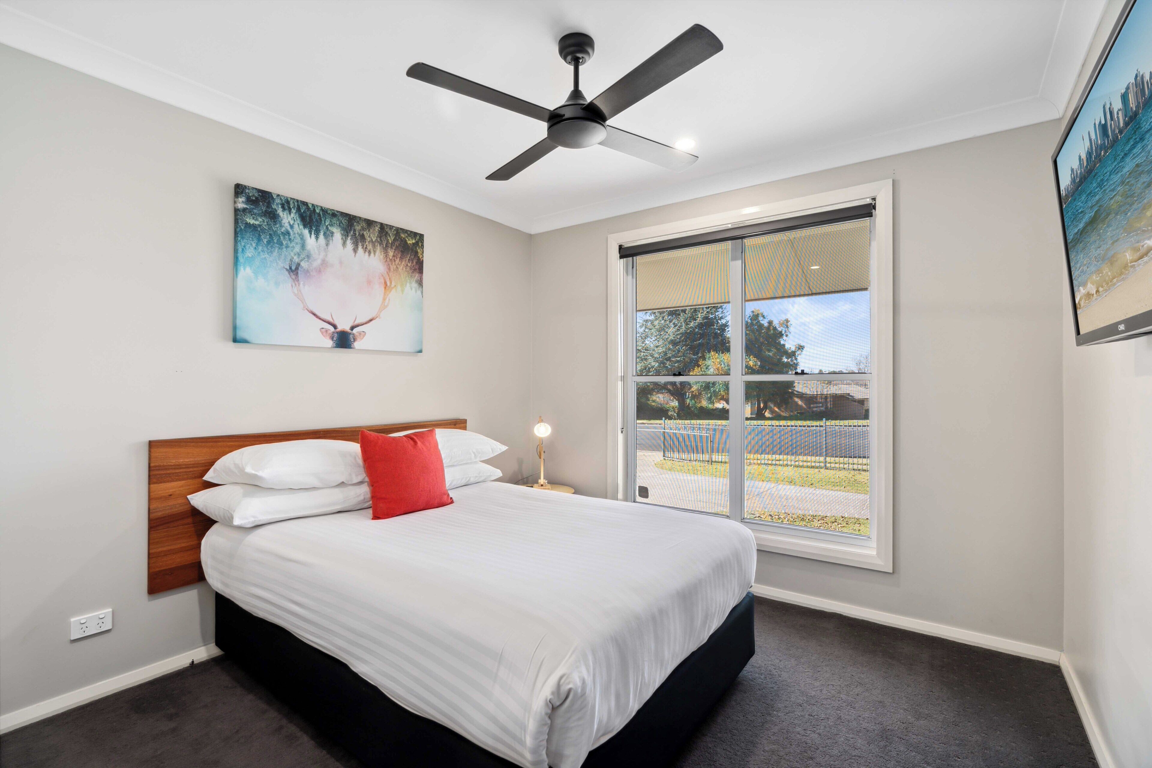 Ein Schlafzimmer mit Bett, Deckenventilator, Fenster mit Blick und einem Bild an der Wand.