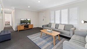 A modern living room with a grey sofa, a wooden coffee table, and a TV on a wooden stand. - West End Motor Lodge (Orange)
