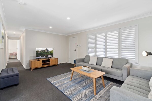 A modern living room with a grey sofa, a wooden coffee table, and a TV on a wooden stand.