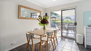 A dining area with a wooden table and chairs, a vase with flowers, a large mirror, and a sliding glass door leading to an outdoor space. - West End Motor Lodge (Orange)