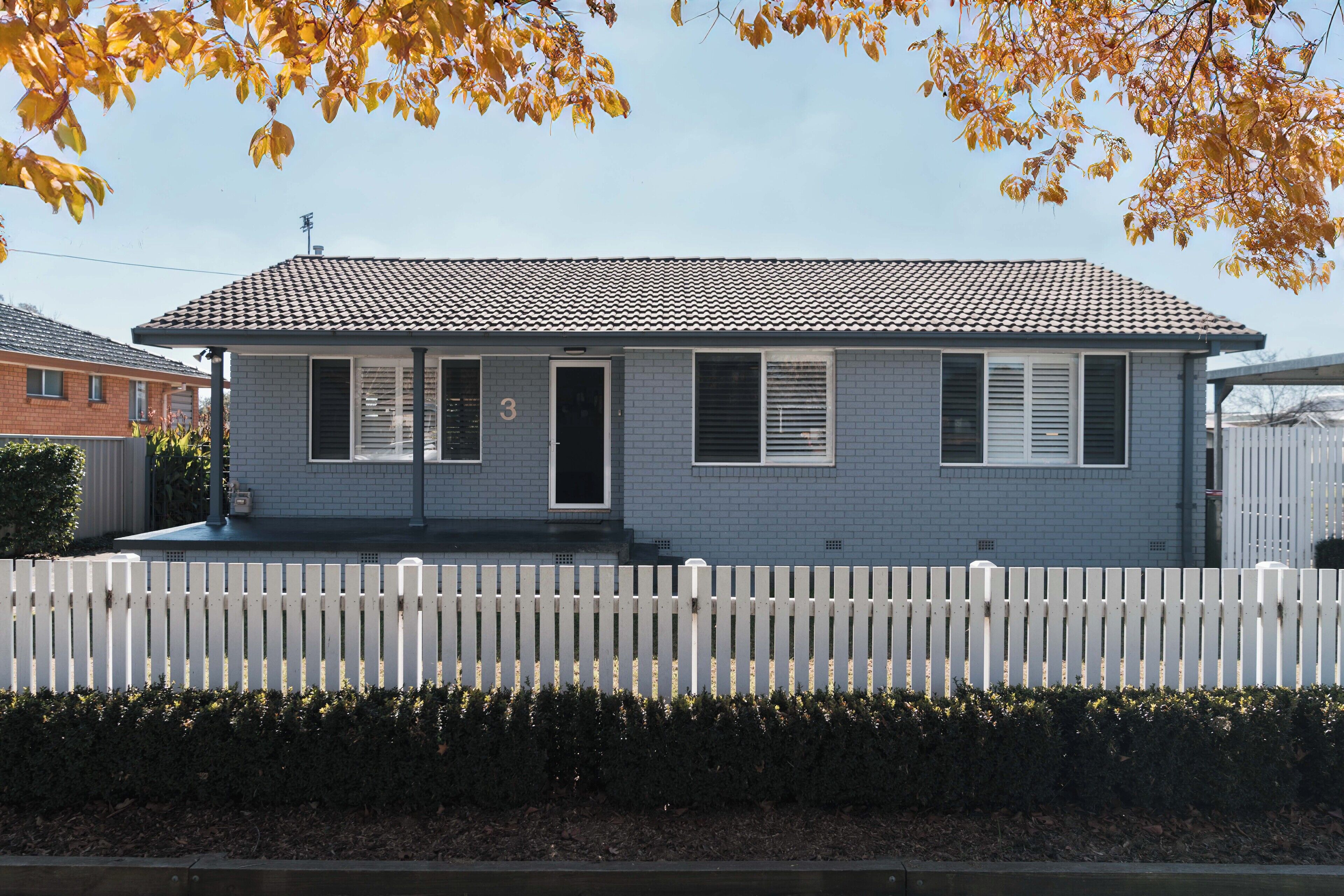 A single-story house with a tiled roof, a white picket fence, and a number '3' on the door.