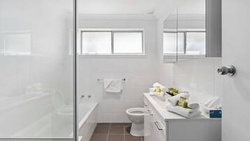 A modern bathroom with a glass shower enclosure, a white toilet, and a vanity with toiletries.