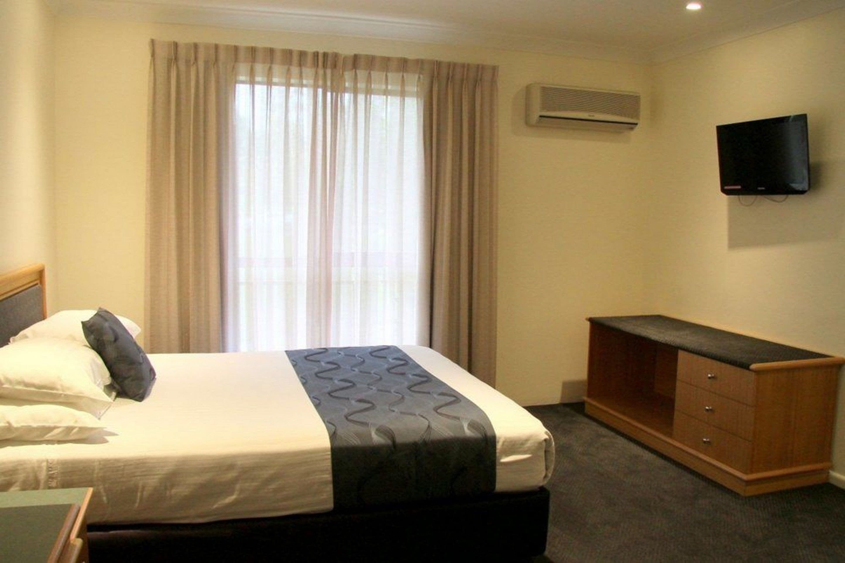 Een hotelkamer met een bed, een aan de muur bevestigde televisie en een raam met gordijnen.