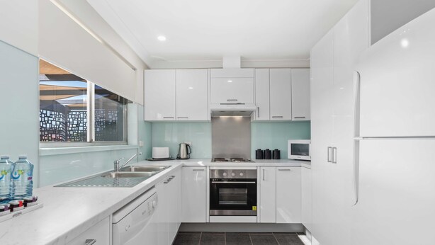 A modern kitchen with white cabinets, a stainless steel oven, and a window overlooking a cityscape. - West End Motor Lodge (Orange)