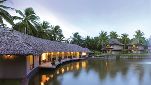 A resort with thatched-roof cottages by a calm lake, surrounded by palm trees. - Coco Lagoon by Great Mount (Anaimalai)