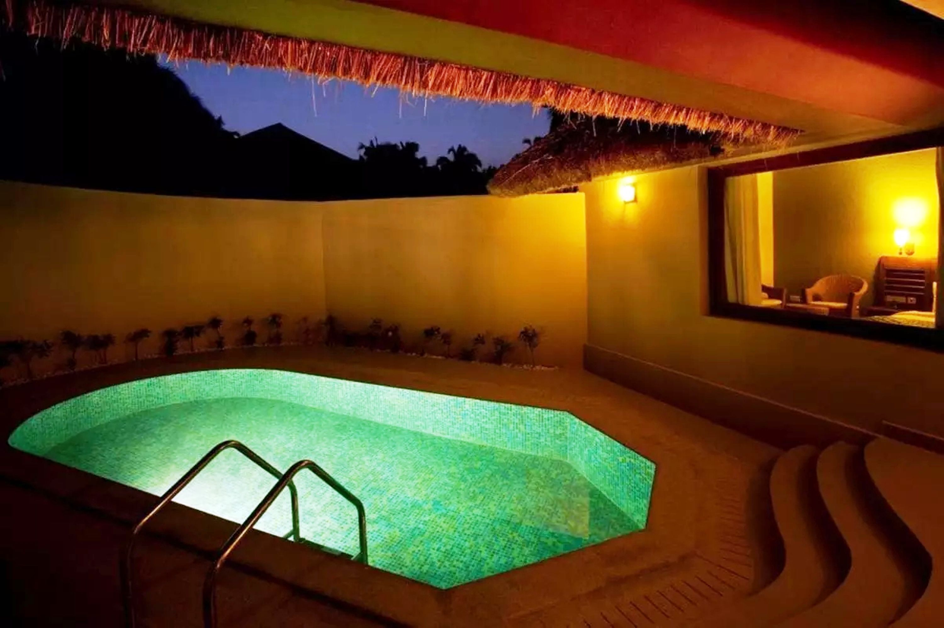 Una piscina con fondo de cristal, rodeada por un muro bajo y un techo de paja.