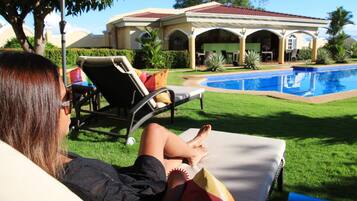 Relax by the serene pool surrounded by lush greenery and a classic building in the background.