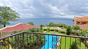 Ein Balkon mit Blick auf ein Schwimmbad, üppiges Grün und ein weiter See.