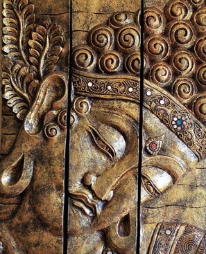 Ein detailliert geschnitztes Holzpaneel mit aufwendigen Verzierungen, darunter floralen Mustern und einer zentralen Figur.