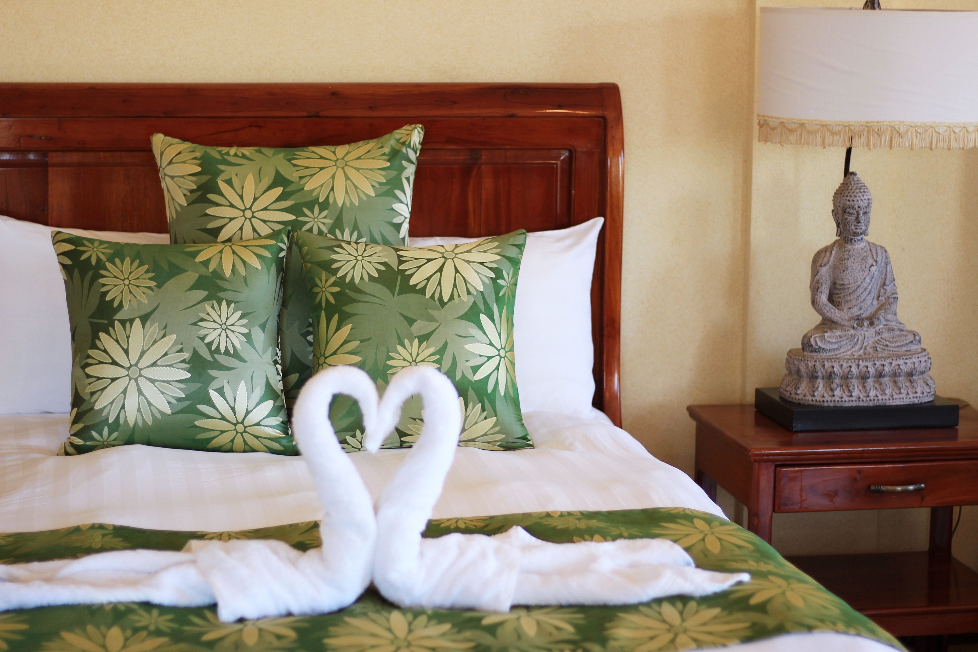 A neatly made bed with green floral pillows and a swan-shaped towel arrangement.