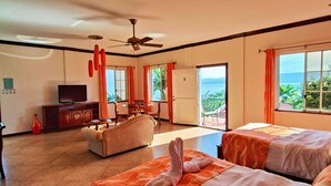 Una habitación de hotel con una cama grande, un sofá, un televisor y un balcón con vista al mar.
