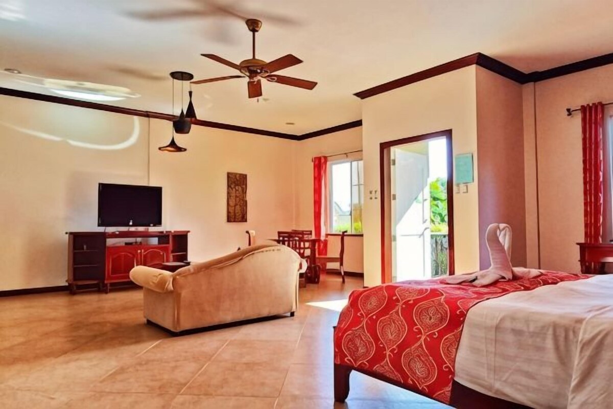 A hotel room with a bed, a sofa, a TV, and a ceiling fan.