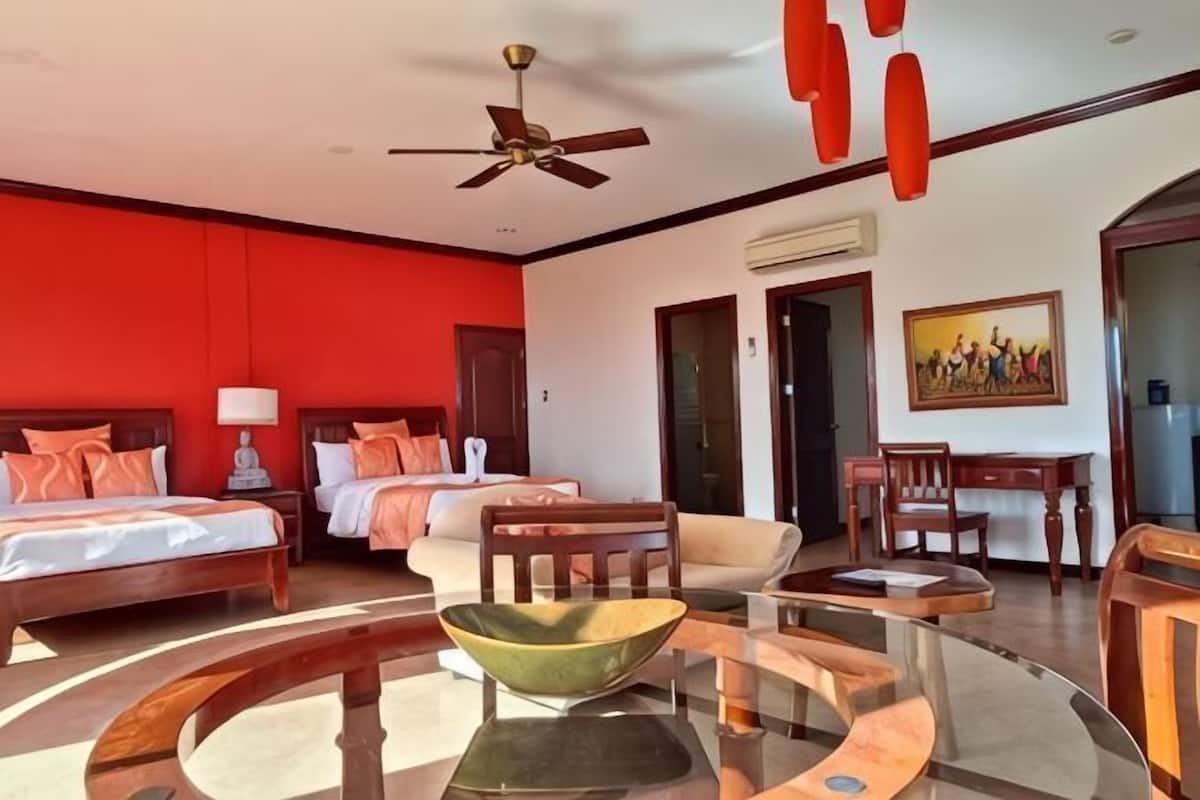 Una habitación de hotel con dos camas, una mesa redonda, un ventilador de techo y un cuadro en la pared.