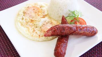 Un plato con huevos revueltos, arroz blanco y salchichas a la plancha, decorado con una rodaja de tomate y una ramita de eneldo.