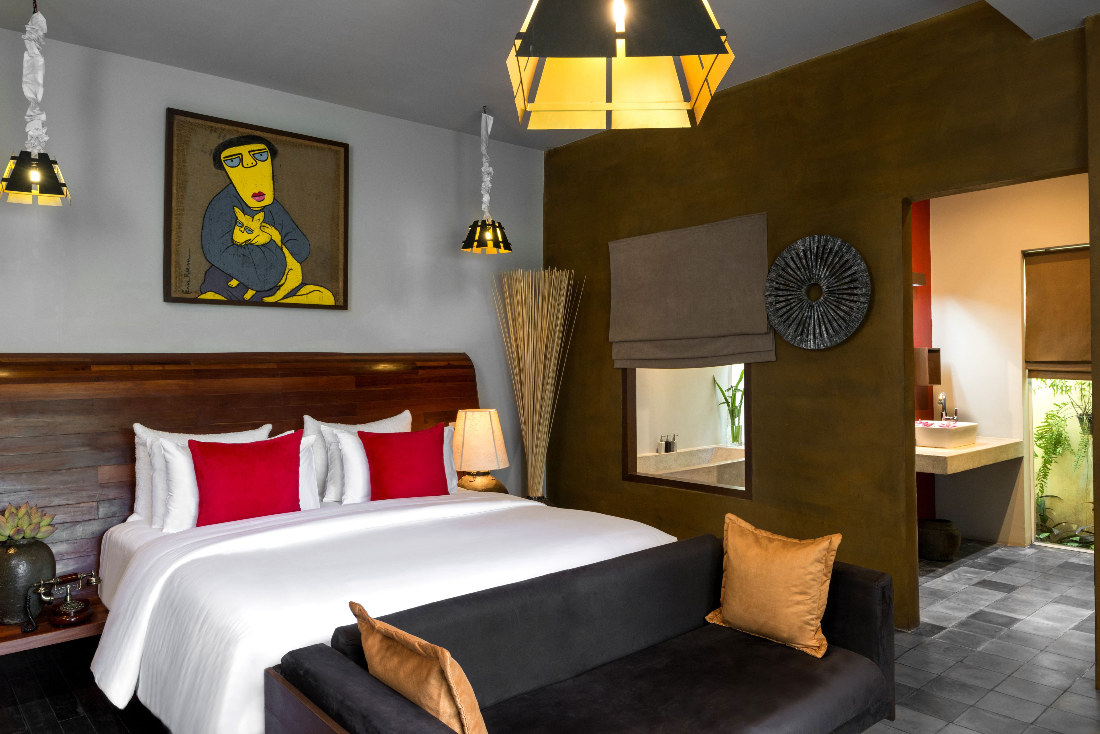 A hotel room with a large bed, a sofa, a painting, a round mirror, and a bathroom visible through an open door.