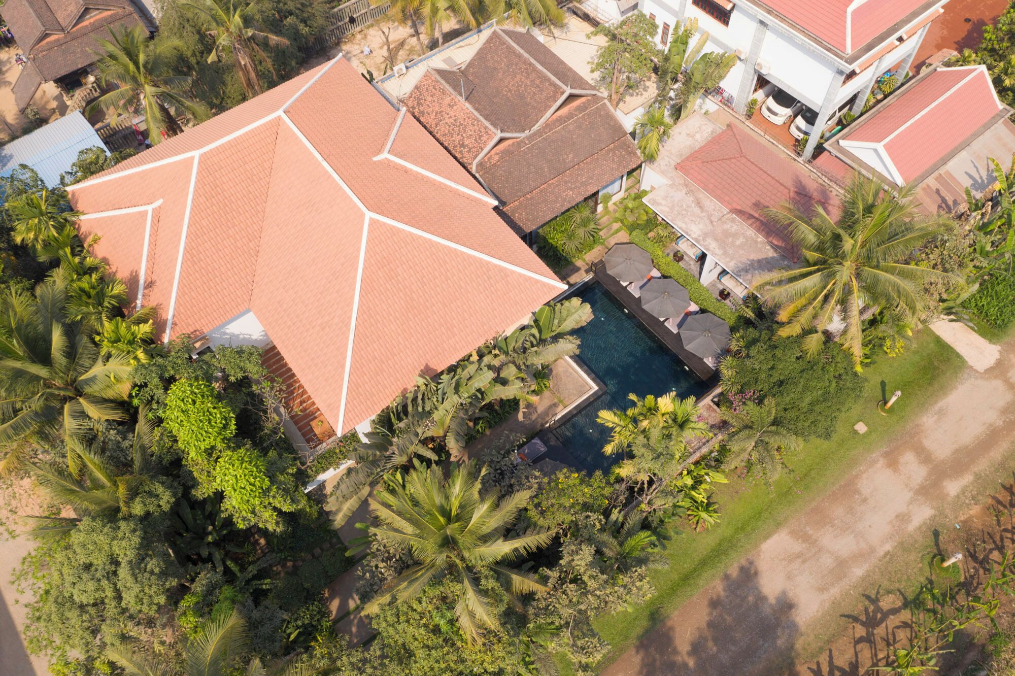 An aerial view of a residential area with multiple houses, a swimming pool, and lush greenery.