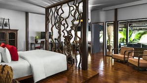 Habitación de hotel moderna con una cama grande, un separador de madera, un rincón de descanso y vistas a un jardín exuberante.