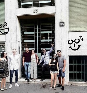 A group of people standing in front of a building with a number 35 on the door and a smiley face with glasses and a plus sign on the wall. - Central Hostel Milano (Milan)