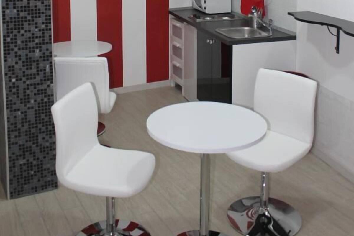 A modern kitchen with red and white striped walls, white furniture, and a small dining area with two white chairs and a round table.