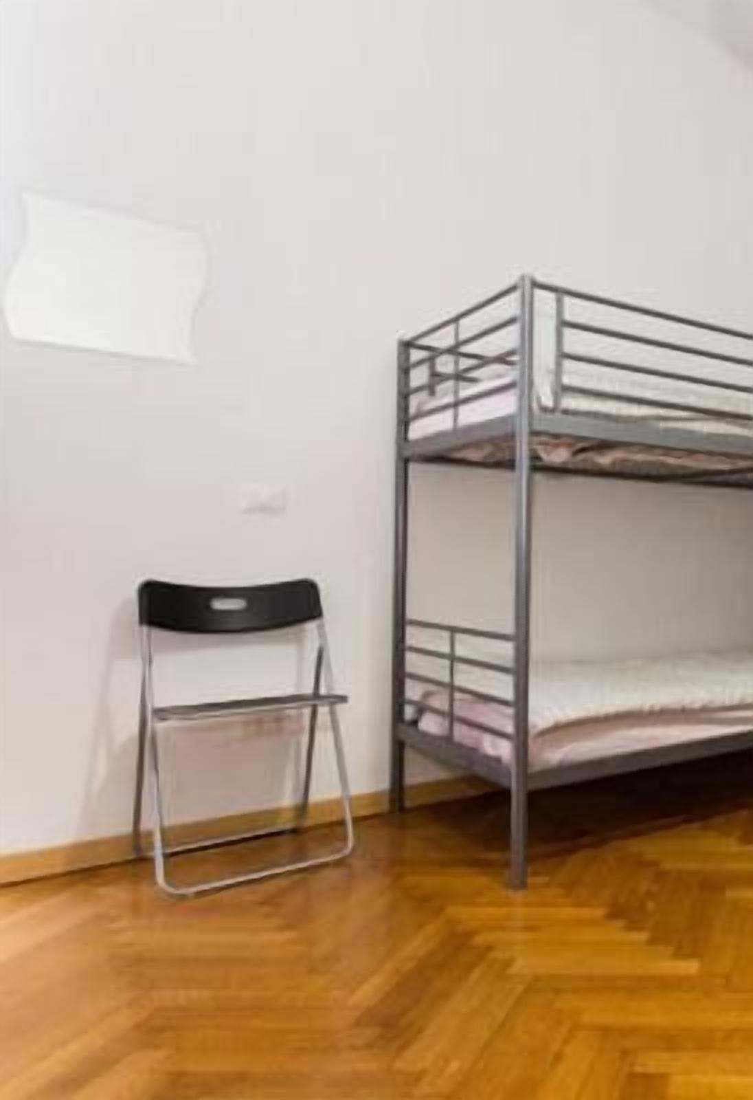 A bunk bed with a foldable chair in a room with wooden flooring and white walls.
