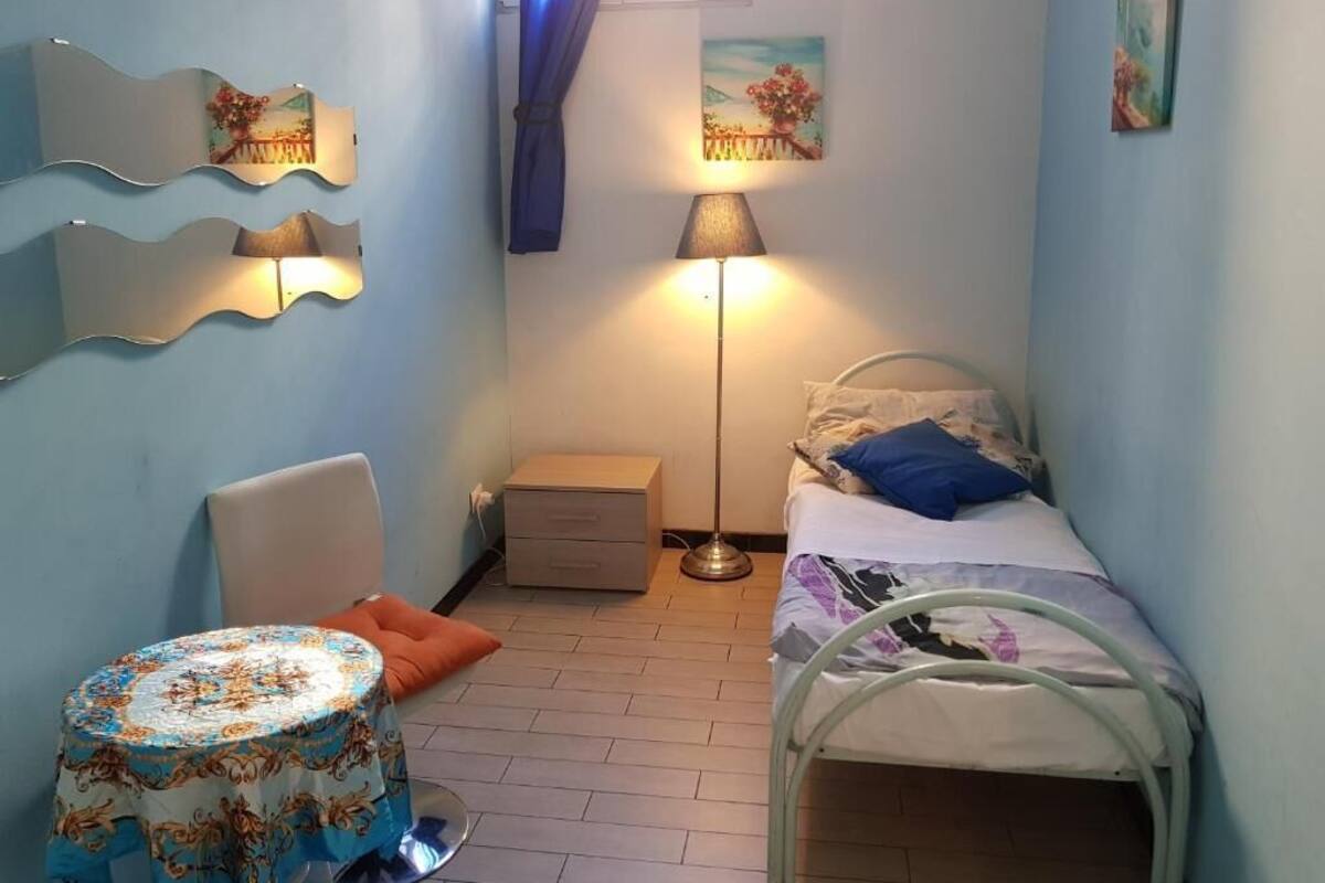 A small, well-lit bedroom with a bed, bedside table, and a lamp.