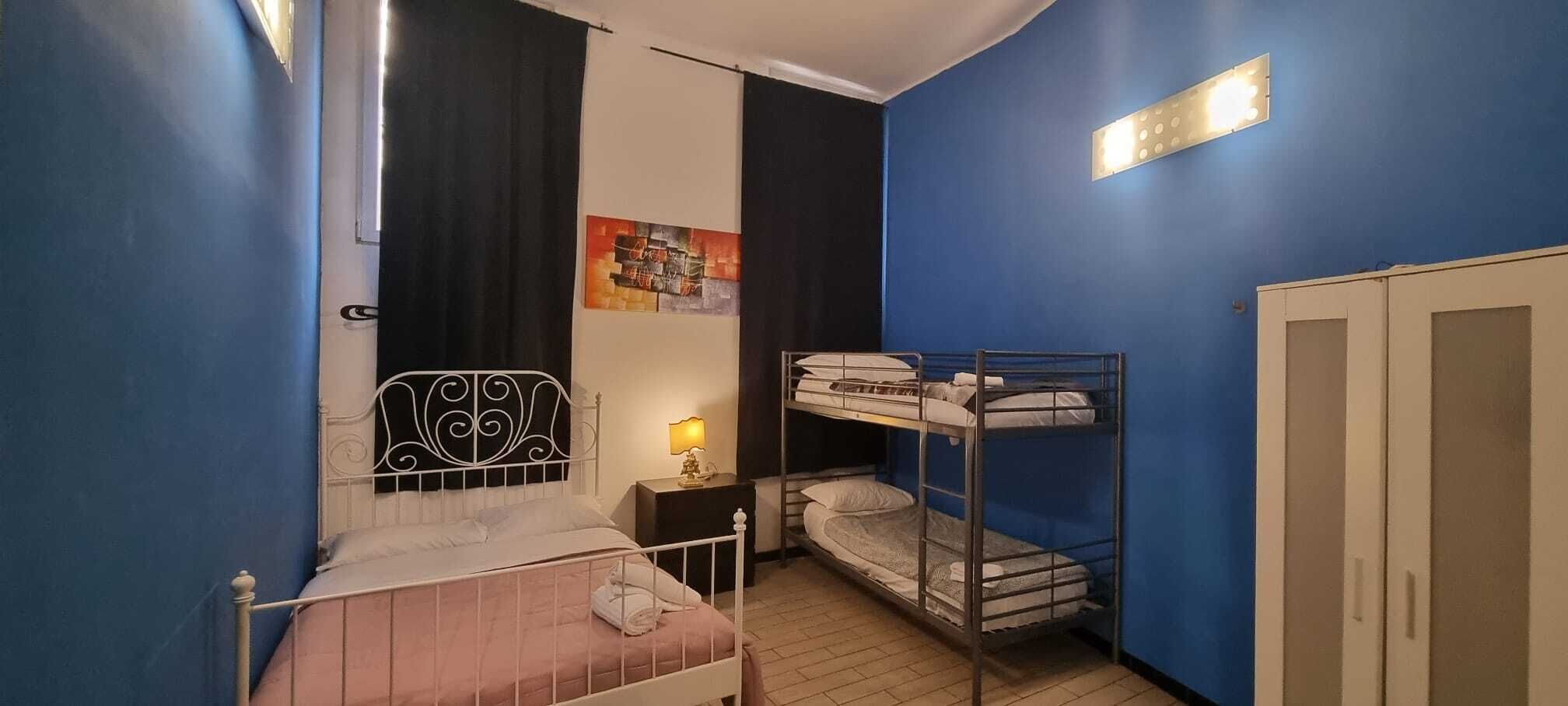 Quarto com uma cama de solteiro, uma cama beliche, uma mesa de cabeceira com abajur, um guarda-roupa e um quadro na parede.