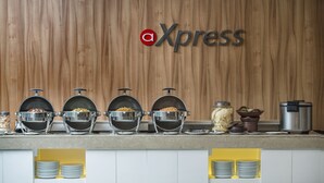Montaje de bufé con varias estaciones de comida, incluyendo un caldo caliente y una olla arrocera, frente a una pared de madera con un logotipo.