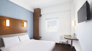 Una habitación de hotel con cama, escritorio, silla, televisión y ventana.