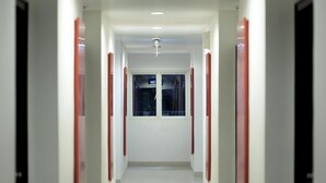 Un pasillo con paredes blancas y detalles en rojo que conduce a una ventana al final.