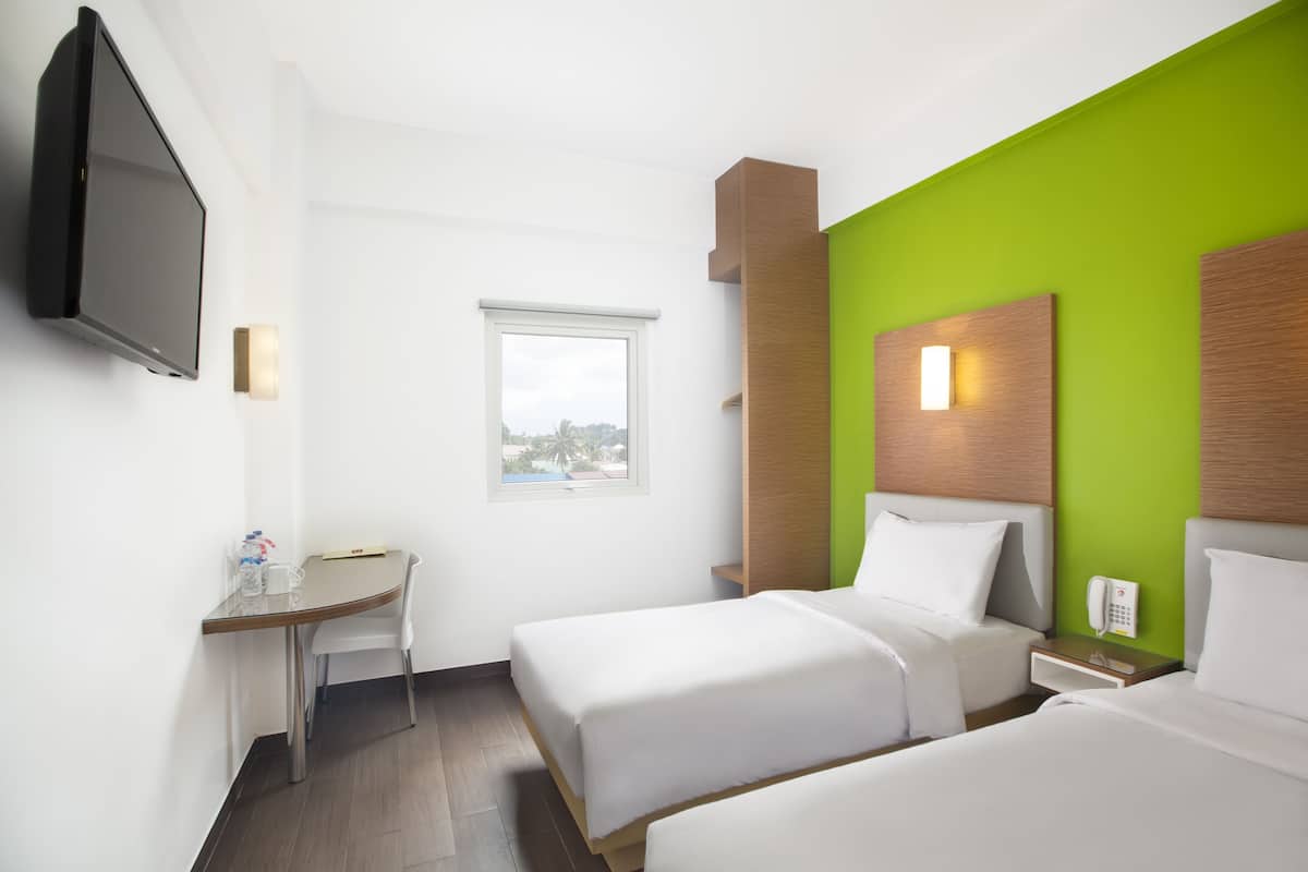 Een hotelkamer met twee bedden, een bureau, een stoel, een televisie en een raam.
