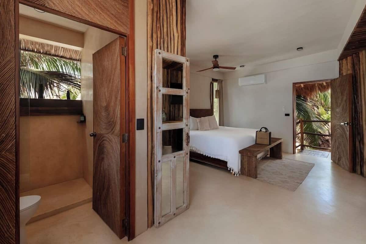 Ein Schlafzimmer mit einem Bett, einer Holztür, einem Deckenventilator und Blick auf Palmen.