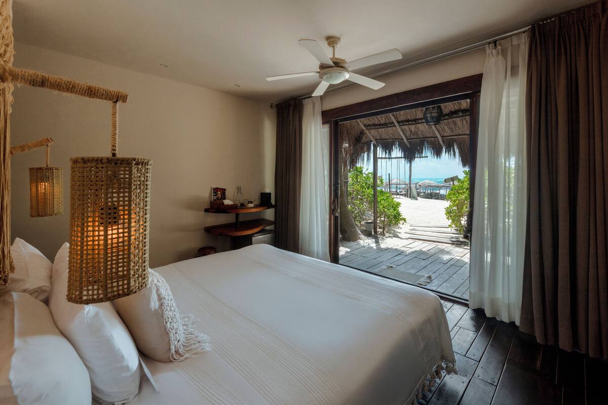 Ein Schlafzimmer mit einem Bett, einem Deckenventilator, einer Korblampe und Blick auf den Strand.
