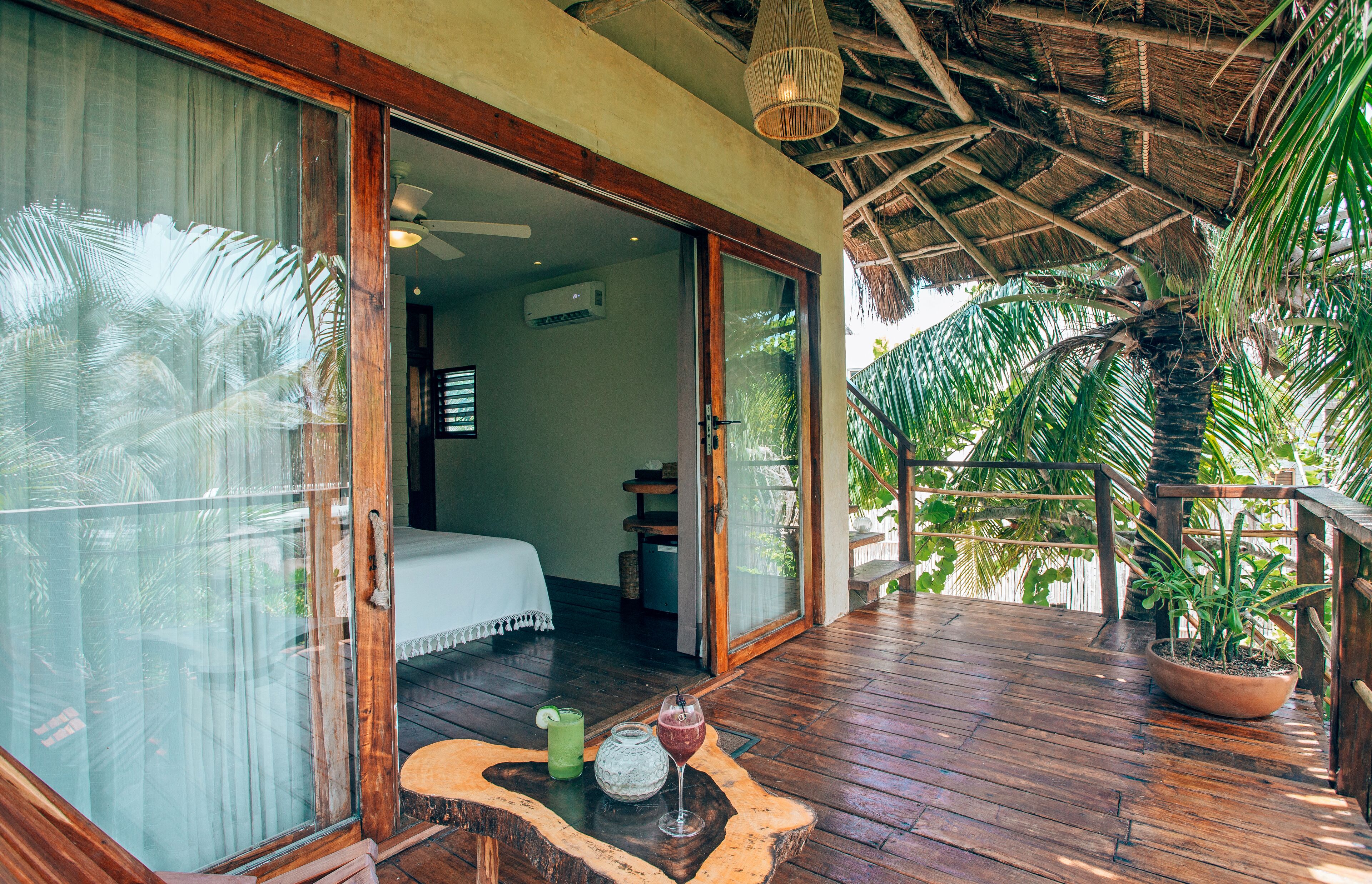 A wooden deck with a thatched roof, a bed, and a potted plant.