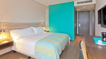 Una habitación de hotel con una cama, mesita de noche, lámpara y una cafetera sobre una mesa de madera.